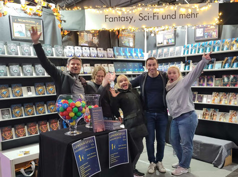 Fünf Personen stehen lachend und ausgelassen zusammen an einem Messestand.