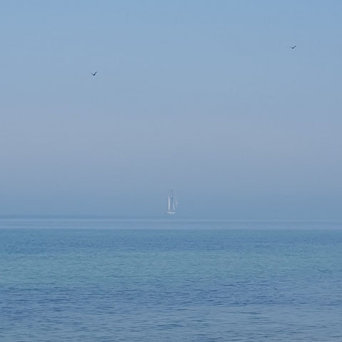 Ein Segelboot schwebt in der Ferne vorbei an dem Tag, wo Himmel und Erde sich berührt haben.