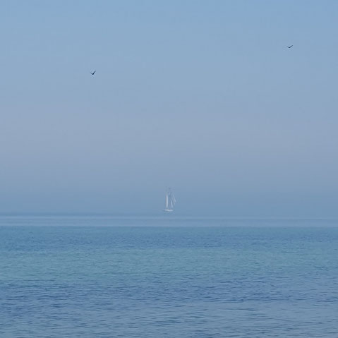 Ein Segelboot schwebt in der Ferne vorbei an dem Tag, wo Himmel und Erde sich berührt haben.