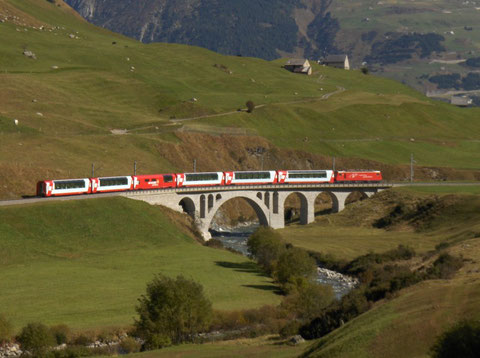 Eine HGe 4/4 vorgespannt an einer Premium-Garnitur des Glacier Express im Urserental vor Hospenthal.