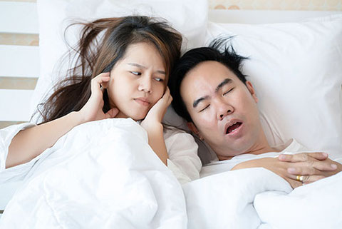 夫婦がベッドで眠っていて、夫のいびきに妻が困っている写真