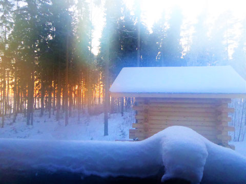 Große Blockbohlen-Außensauna mit Fenstern zum See, Südseite und nach Westen (Sonnenuntergang) sowie mit schwerem, holzbefeuertem Steinofen mit Glastür und Warmwasserboiler im Kamin.