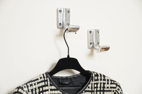 Patère ou crochet mural vintage des années 50 en aluminium présenté sur un mur beige avec cintre noir et veste quadrillée noir et blanc