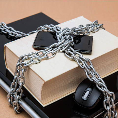 Ein Buch, ein Notebook und ein Smartphone sind mit Ketten verschnürt