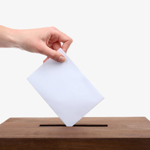 Eine Hand wirft ein Kuvert in eine Wahlurne