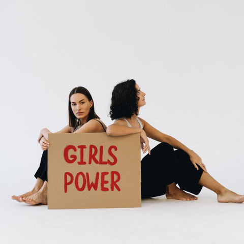 Zwei Frauen sitzen hinter einem Girls Power-Schild