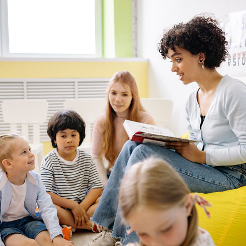 Eine Kindergärtnerin liest Kindern aus einem Buch vor