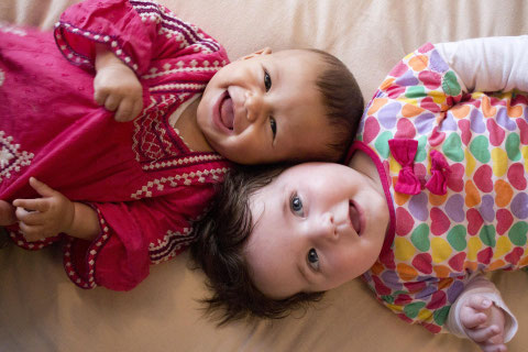Zwei fröhlich lachende Babys in bunter Kleidung, die eng aneinander auf dem Boden liegen und sich sichtlich wohl fühlen, symbolisch für FenKid Kurse bei mein schützling in München Schwabing