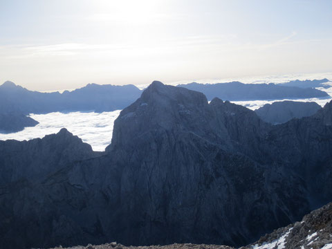 Der Jalovec vom benachbarten Mangart (2.679m) aus gesehen, beim tiefen Einschnitt vor dem Nebelmeer, dem Kotsattel (Kotovo sedlo) beginnt der Klettersteig über den Nordwestgrat auf den Gipfel des Jalovec