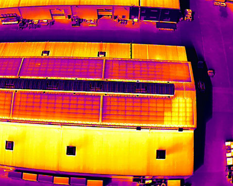 Thermografische Drohnenaufnahme einer Photovoltaikanlage auf einem Industrie- und Hallendach zur Erkennung von Hotspots und Moduldefekten.