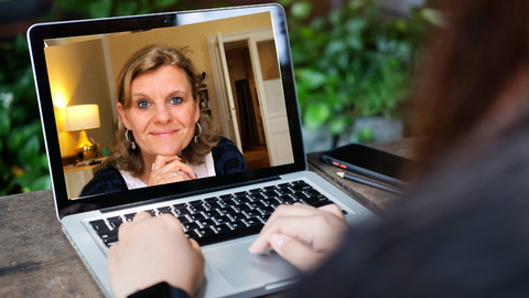 Eine Frau nimmt an einer Online-Sitzung teil, auf ihrem Laptopbildschirm ist das lächelnde Gesicht einer Beraterin zu sehen, was eine freundliche und persönliche Beratungsatmosphäre vermittelt.