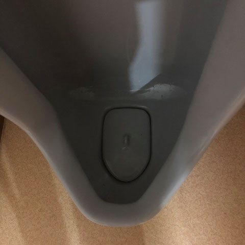 清掃前の男子便器の写真。表面はきれいだが、蓋を開けると強い臭いがあり、内部に尿石が溜まっていた状態。