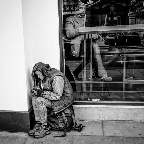 Streetphoto: Eine Obdachlose sitzt vor einem Café