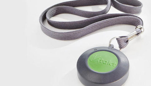 Funksender von Vitakt Hausnotruf mit grünem Knopf auf einem grauen Nylon-Band