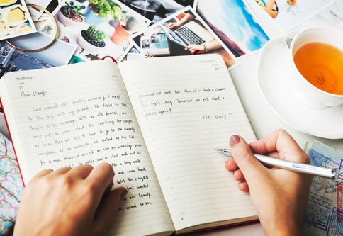 Manos escribiendo en un diario junto a una taza de té, símbolo de ejercicios de escritura para mejorar el vocabulario y la gramática en español.