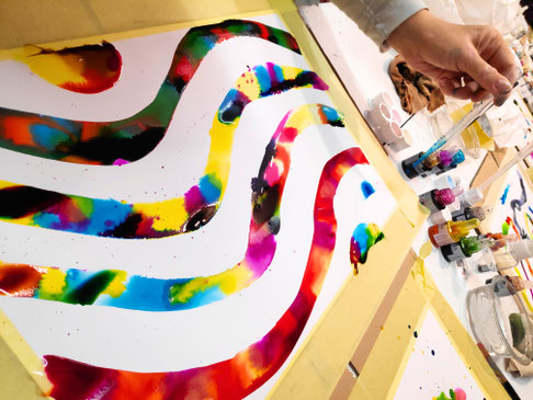 Bunte Linien in Aquarellfarben und eine Hand, die Farbe auf das Papier tropft
