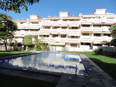 Apartmenthaus mit viel Sonne und im Vordergrund sieht man die Poolanlage der Gemeinschaft.