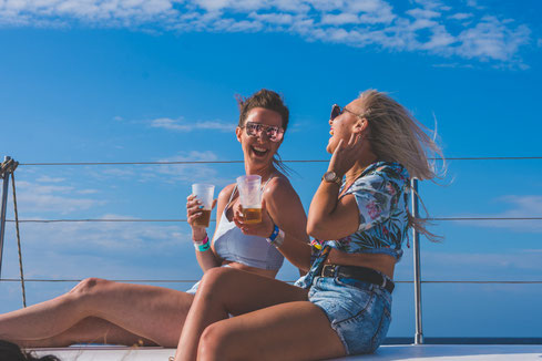 two women on a yacht in the sun, with drinks in their hands