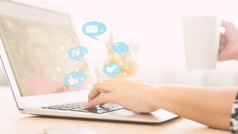 Mains de femme sur un clavier d'ordinateur portable, avec des pictogrammes de boîte mail, de like et de panier de site e-commerce.