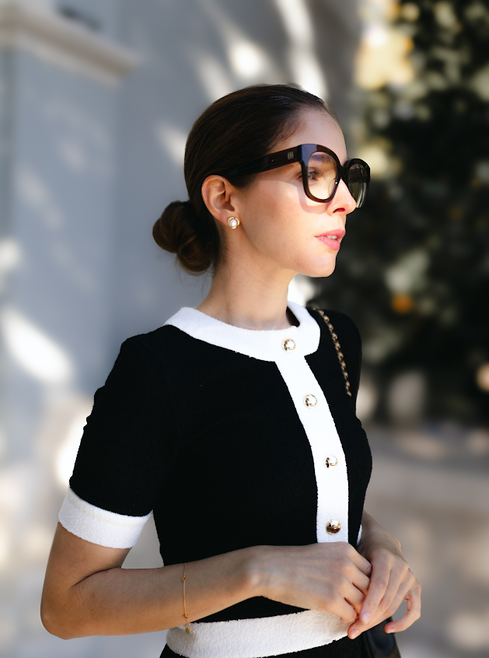 Frau im eleganten schwarz-weißen Kleid mit großen Sonnenbrillen und Perlenohrringen im warmen Tageslicht.