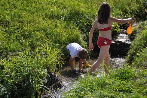 Kinder spielen am Naturbächlein vor dem Haus