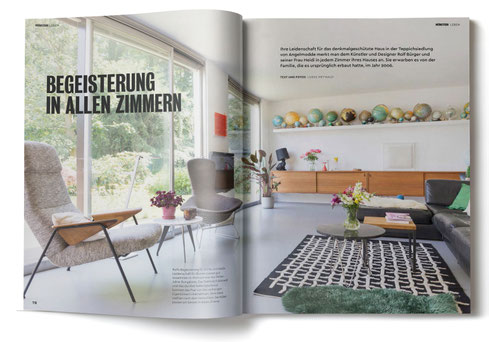 Blick in das Wohnzimmer eines Hauses der Teppichsiedlung Angelmodde. Eine lange Fensterfront links, ein schwarzes Sofa rechts. Im Hintergrund ein Sideboard und ein Board mit vielen Globen