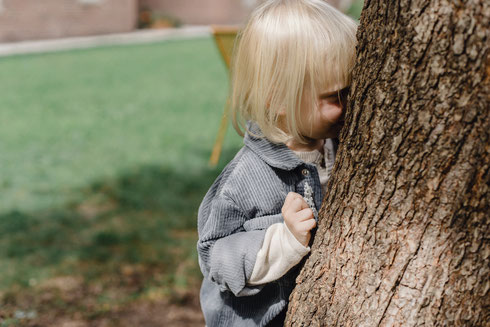 Kind versteckt sich hinter Baum