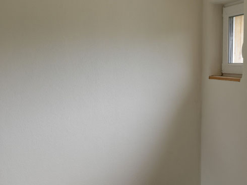 Gestrichene Wandfläche mit Lehmfarbe, bei der Licht und Schatten die Farbwirkung im Raum verändern.