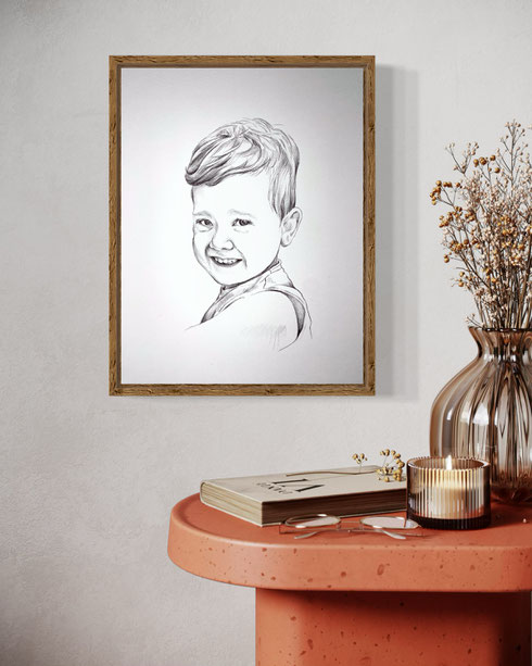 In opdracht gemaakte portrettekening van een lachend jongetje, met pen getekend in realistische stijl. De tekening hangt in een houten lijst aan een lichte muur, naast een terracotta tafel met decoratieve objecten.