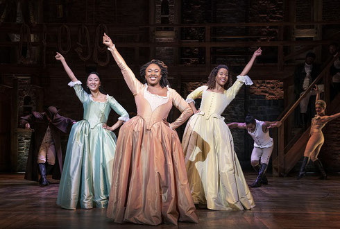 Three Female members of the cast on stage at a performance of Hamilton