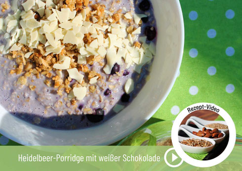 Heidelbeer Porridge mit Knuspermüsli und weißer Schokolade auf einer grünen Tischdecke in einer weißen Schüssel