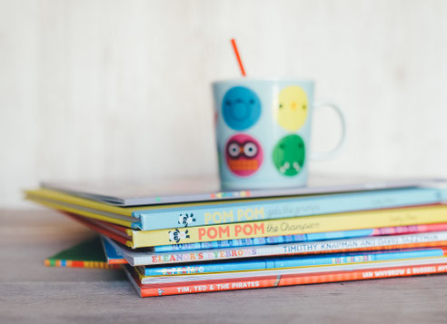 colourful books in a bile, with a mug with smiley faces on it