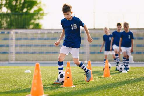 Jugendliche dribbelt auf dem Rasen mit dem Ball zwischen den Pylonen