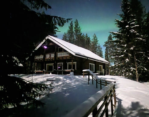 Ferienhaus in Lappland im Winter unter Nordlichtern – gemütliches Blockhaus im Schnee