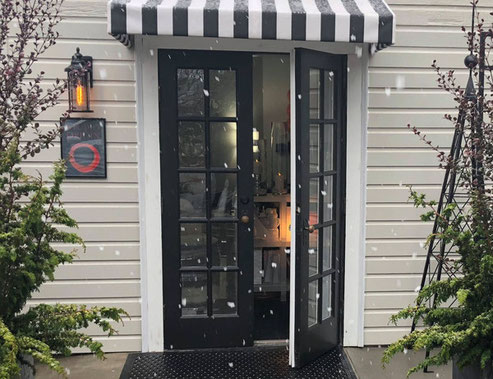 Photo showing the doors to STUDIO ORIGIN Intimate Garden Pilates Studio located in Newberg Oregon, in a chilly beautiful snow flurry. Black double doors, one slightly open to with a warm inviting soft lit glow inside.