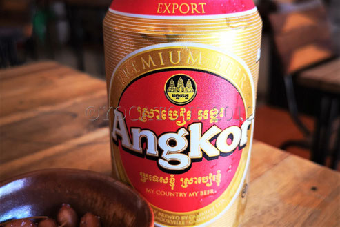 Une canette de bière Angkor posée sur une table avec des cacahuètes
