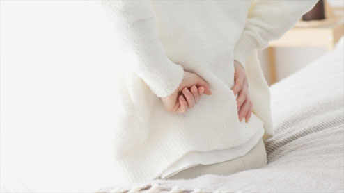 朝起きた時に腰を押さえて痛みに悩む女性のイメージ