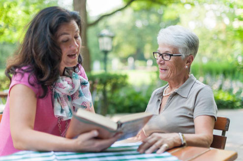 Senioren-Assistentin liest einer Seniorin vor.