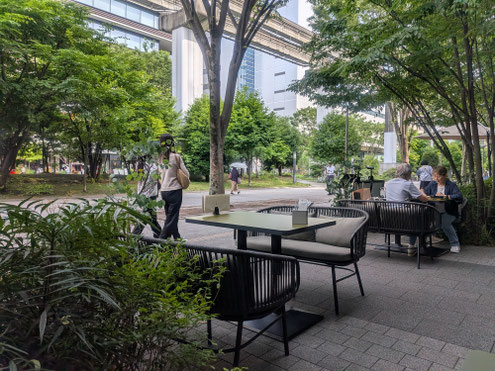 立川市のGREEN SPRINGSの店舗席から見た、緑に囲まれたテラス席と歩道の風景。立川でのお見合い後のお茶や交際中のデートに使いやすい、落ち着いて会話できるデートスポットのイメージ