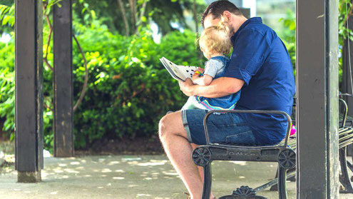 子供を膝にのせて本を読み聞かせる父親