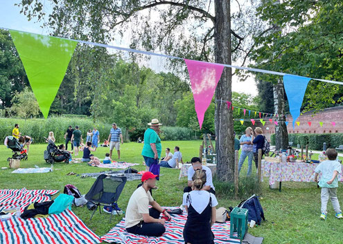 Personen bei einem Picknick mit Decken im Glacis-Park. Zwischen den Bäumen ist eine bunte Girlande gespannt.