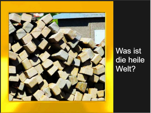 Dieses Foto zeigt ein Chaos an Bahnschwellen, die unsortiert abgelegt wurden. Um das Foto wurde ein Goldrahmen gelegt. Der Titel: Was bedeutet die "heile Welt"?