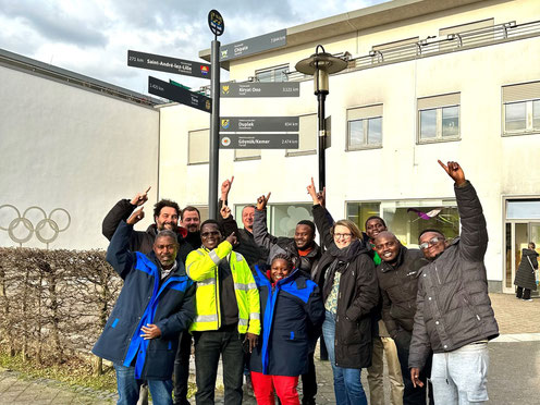 Gruppenfoto mit allen Projektbeteiligten, allen Personen zeigen auf einen Wegweiser nach Chipata.