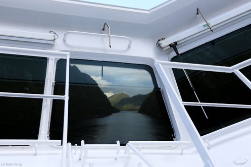 The Trollfjord is reflected in a front window of the command bridge.