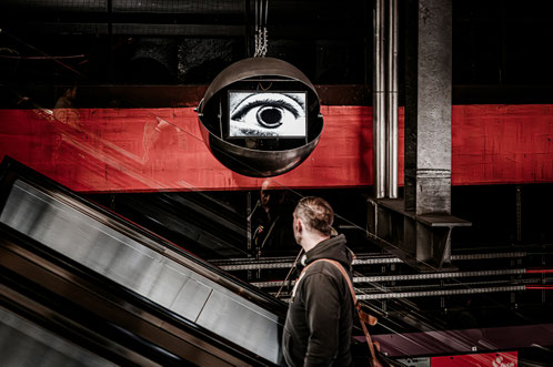man-looks-up-at-a-surveillance-camera-displaying-an-eye