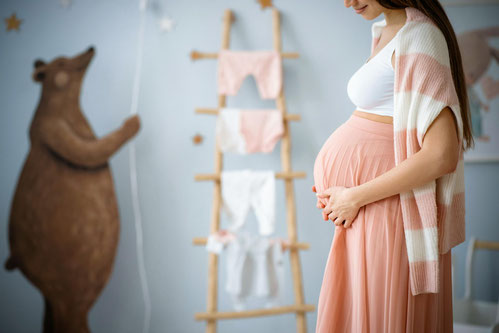 Schwangere Frau streichelt sich im bereits eingerichteten Kinderzimmer ihren Babybauch