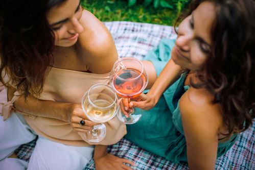 Zwei Freundinnen stoßen gemeinsam beim Picknick mit Wein an