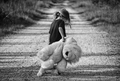 Mädchen mit großem Teddy läuft eine Landstraße entlang.