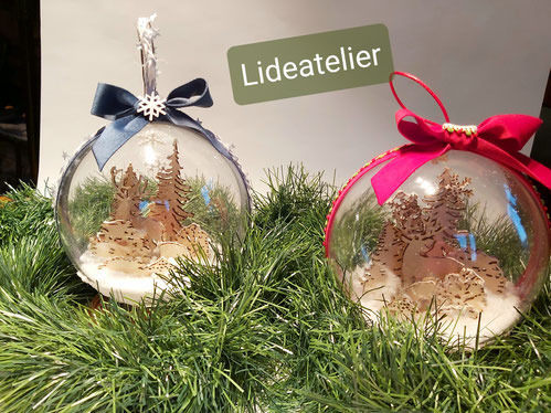 2 boules de noel de diametre 14 cms en plexiglas a l'interieur :  un cerf une biche et des sapins en bois. Le ruban est en velour bleu sur l'une rouge sur l'autre. creation artisanale lideatelier chambery savoie