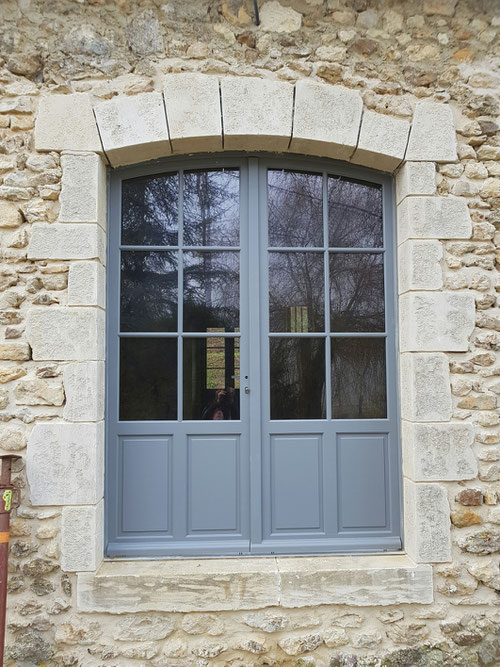 Ouverture pierres de taille avec cintre en arc surbaissé. H 2.45 L 1.60 Pose de menuiserie bois avec soubassement à panneaux à plates bandes et vitrages 6 carreaux égaux proportionnés toujours plus haut que large